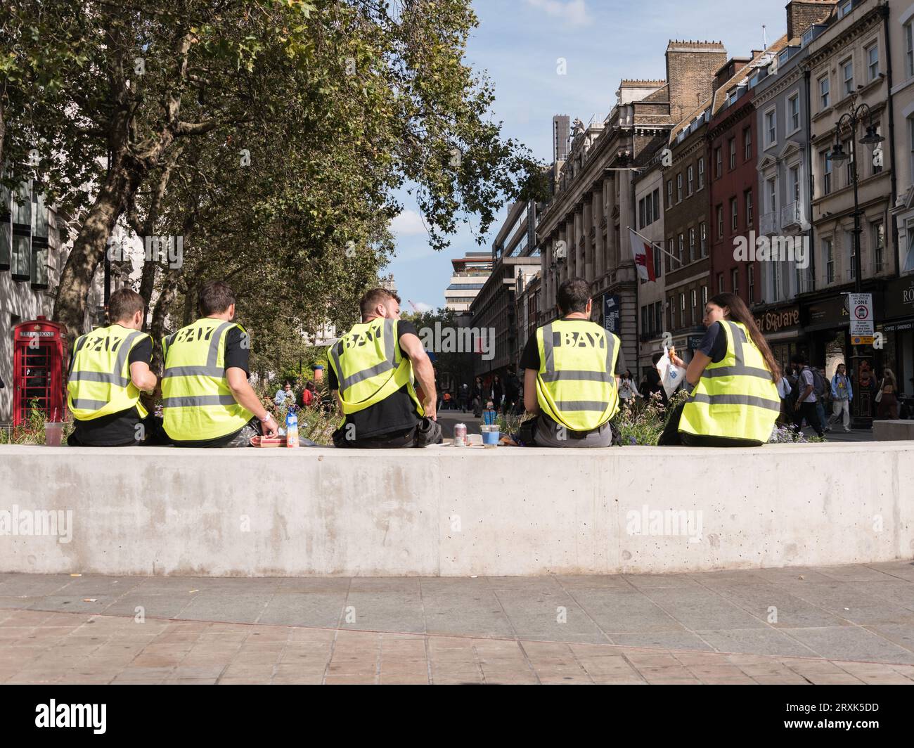 Junge Männer und Frauen, die eine Mittagspause einlegen, während sie Warnwesten von Bay tragen, The Strand, London, England, Großbritannien Stockfoto