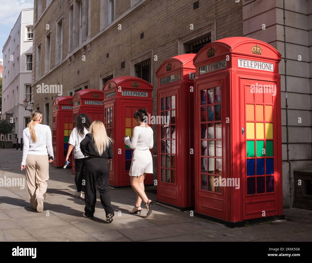 Eine Gruppe junger Frauen besteht an klassischen K6-Telefonboxen, die mit LGBTQ-Regenbogenfarben dekoriert sind, in Broad Court, Covent Garden, London, England, Großbritannien Stockfoto