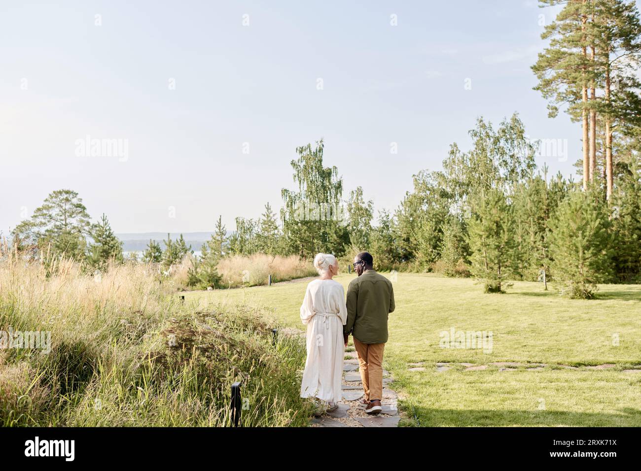 Rückansicht des älteren Paares, das die Hände hält und seinen Spaziergang im Park genießt Stockfoto