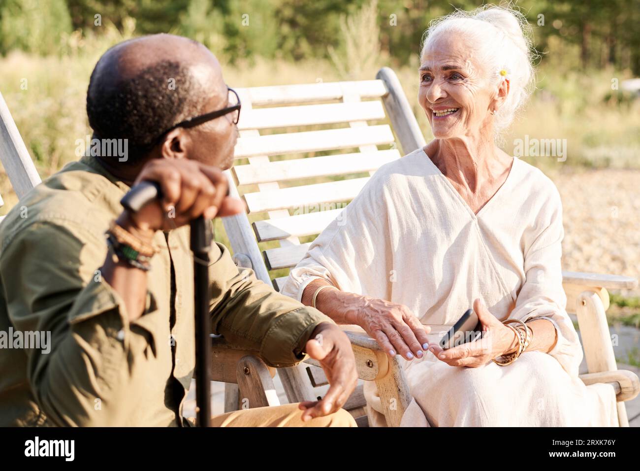Glückliche ältere Frau, die mit dem Mann spricht, während sie draußen auf Stühlen ruhen Stockfoto