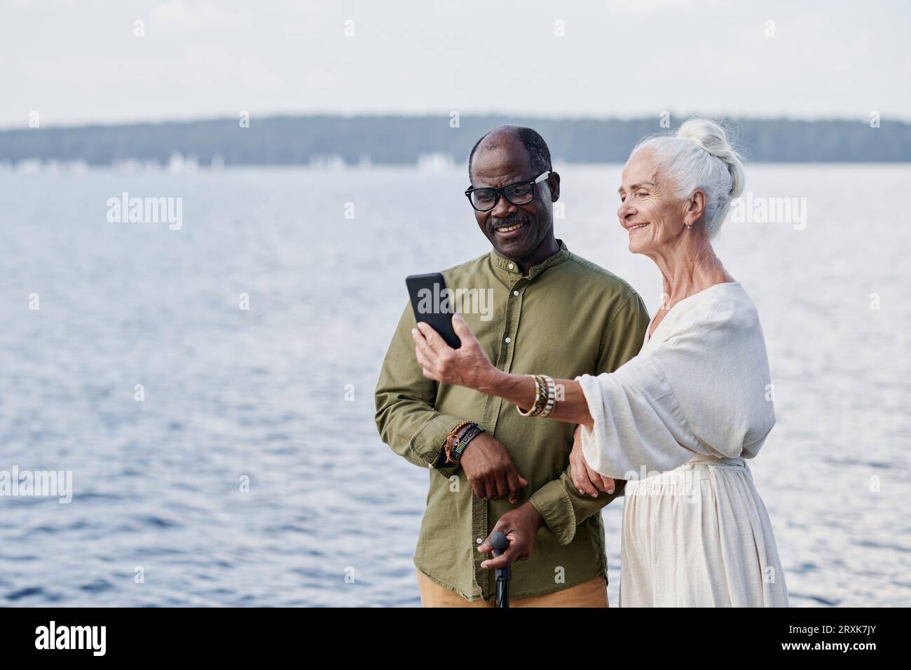 Älteres Paar macht Selfie-Porträt am Telefon am See draußen Stockfoto