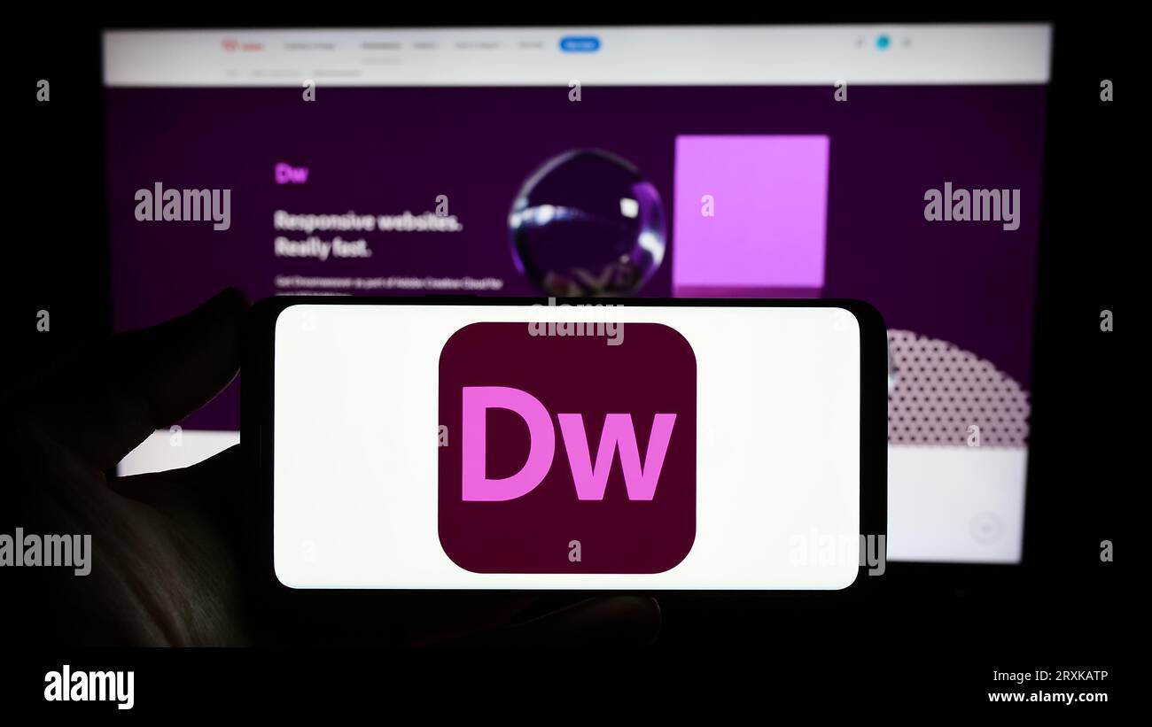 Person, die ein Smartphone mit dem Logo der Webentwicklungssoftware Adobe Dreamweaver auf dem Bildschirm vor der Website hält. Konzentrieren Sie sich auf das Display des Telefons. Stockfoto