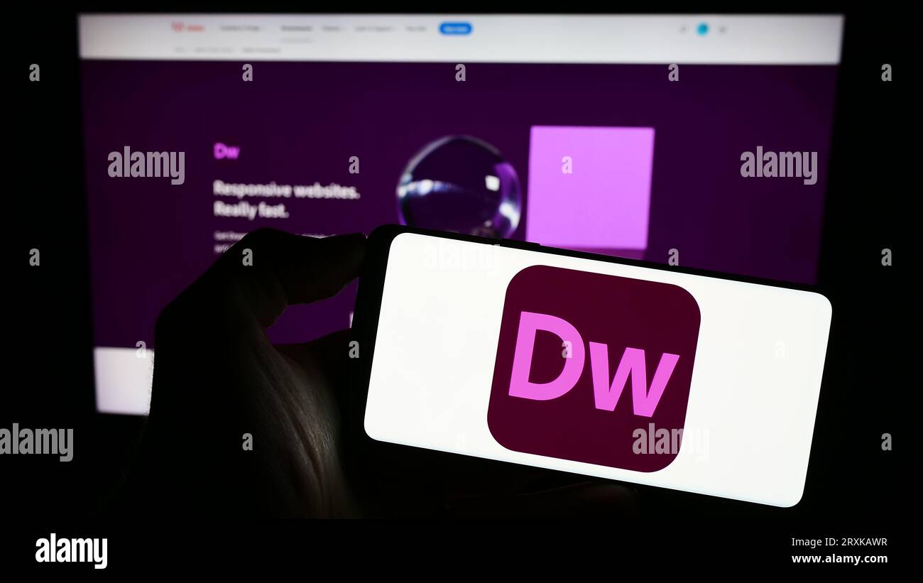 Person, die ein Mobiltelefon mit dem Logo der Webentwicklungssoftware Adobe Dreamweaver auf dem Bildschirm vor der Unternehmenswebseite hält. Konzentrieren Sie sich auf das Display des Telefons. Stockfoto