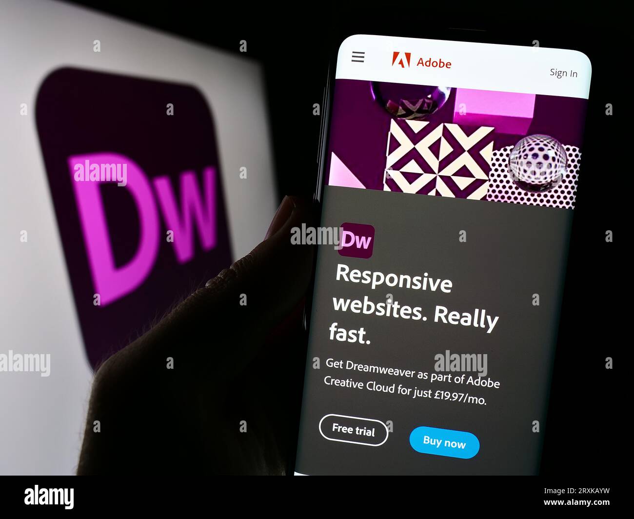 Person, die ein Smartphone mit einer Webseite der Webentwicklungssoftware Adobe Dreamweaver auf dem Bildschirm vor dem Logo hält. Konzentrieren Sie sich auf die Mitte der Telefonanzeige. Stockfoto
