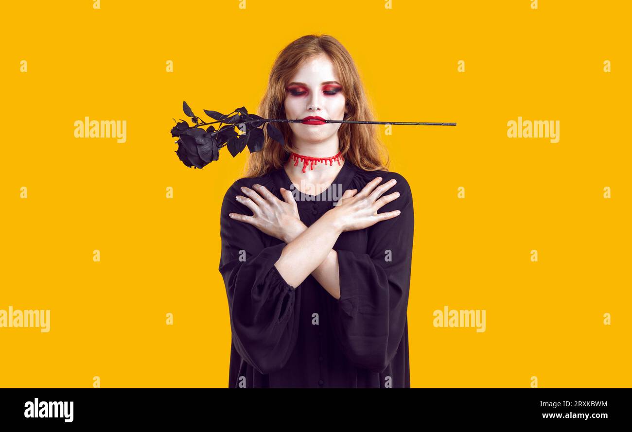 Junge Frau im gruseligen Halloween-Kostüm, mit Blut am Hals und schwarzer Rose im Mund Stockfoto