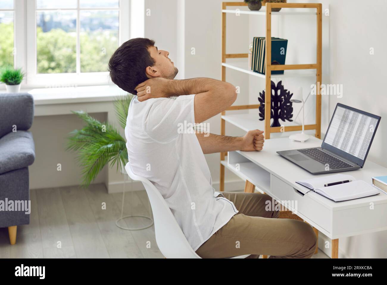 Ein junger Geschäftsmann, der erschöpft aussieht, massiert seinen Hals, während er am Arbeitsplatz sitzt. Stockfoto