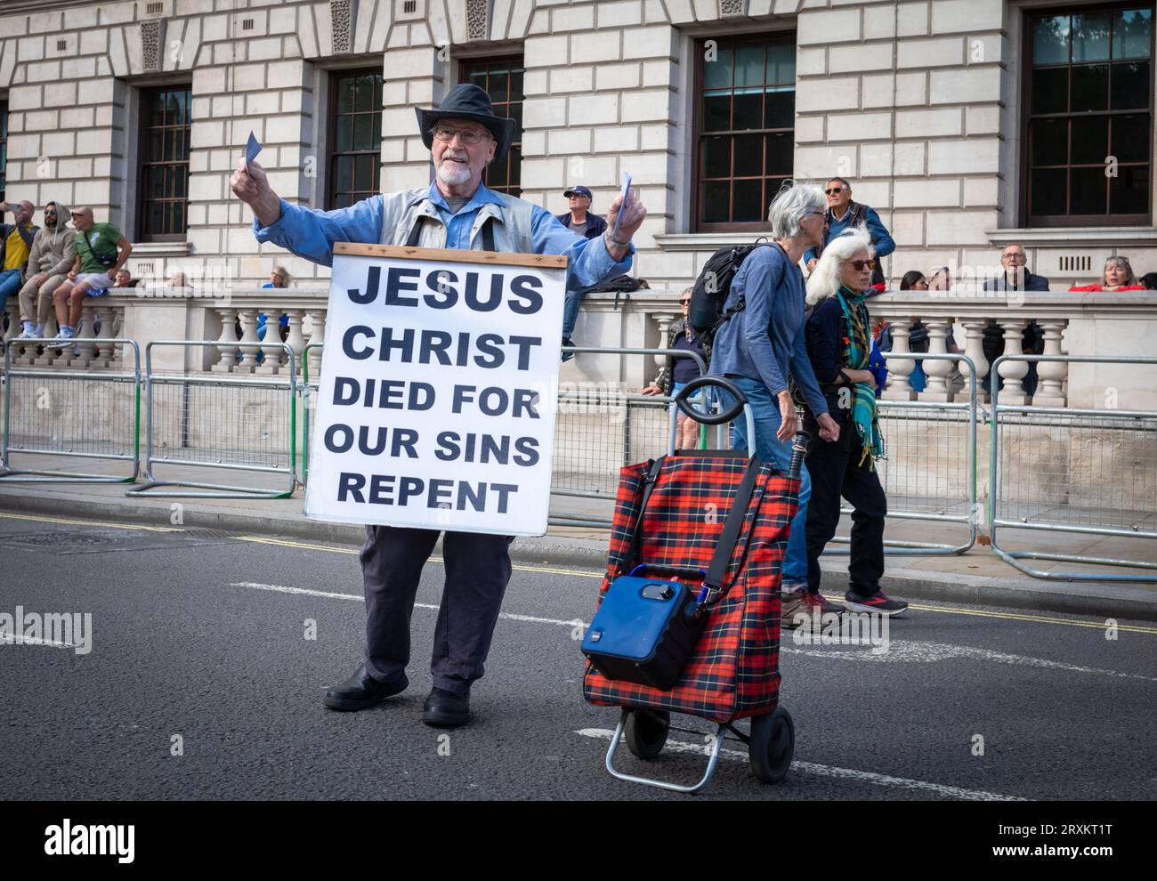 Ein männlicher christlicher Evangelist mit Lautsprecher und Einkaufswagen trägt ein Plakat mit der Aufschrift „Jesus Christus starb für unsere Sünden Buße“ und demonstriert darin Stockfoto