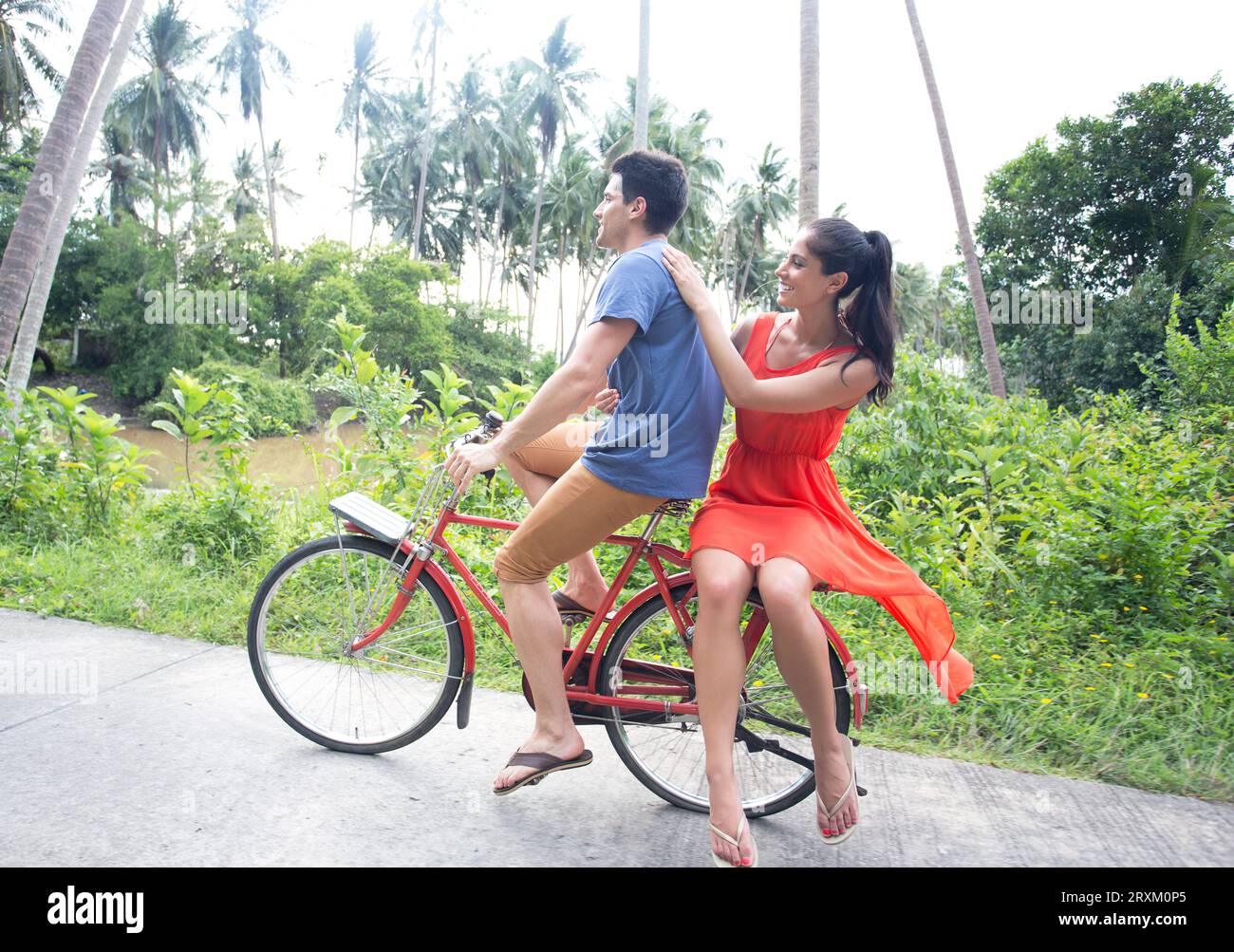 Paare, die Tandemfahrräder in tropischer Umgebung fahren Stockfoto