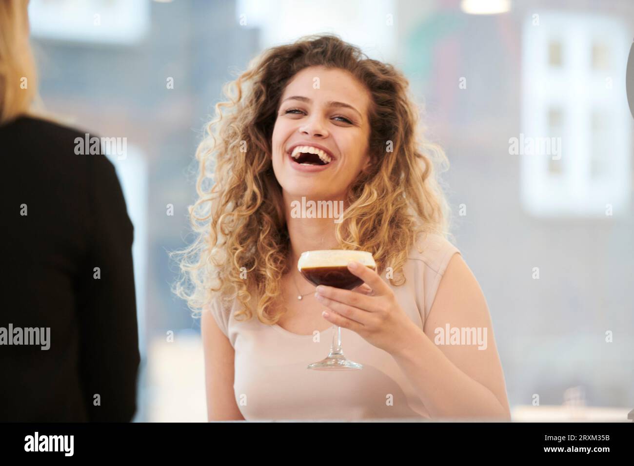 Lachende junge Frau mit Espresso Martini Stockfoto