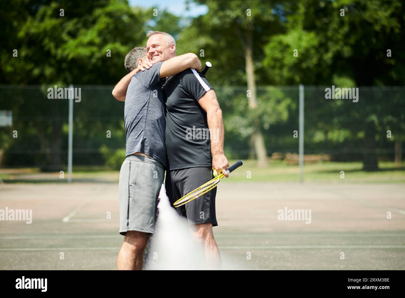 Reifes Paar, das sich auf dem Tennisplatz umarmt Stockfoto