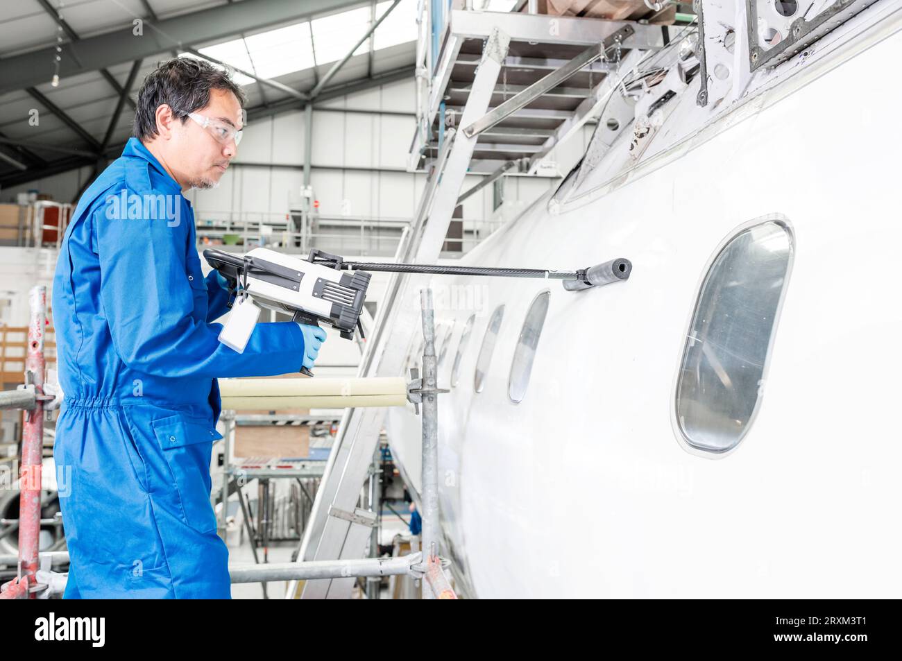 Mann, der im Hangar ein Elektrowerkzeug im Flugzeug benutzt Stockfoto