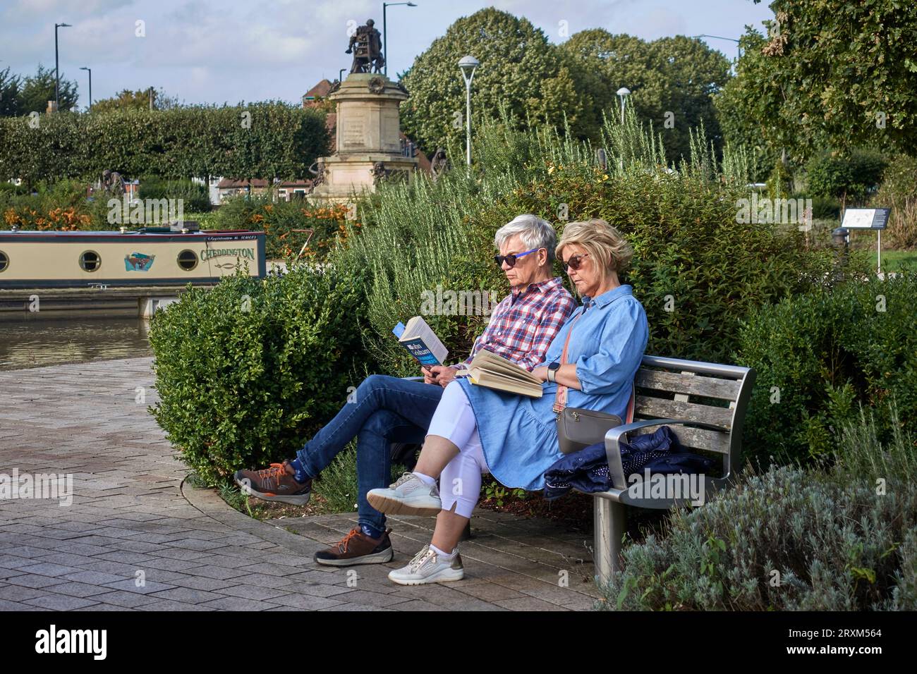 Ehepaar, die Buch im Freien lesen, saßen auf einer Bank in Stratford upon Avon, Warwickshire, England. Zweisamkeit, wie gesinnte Menschen Stockfoto