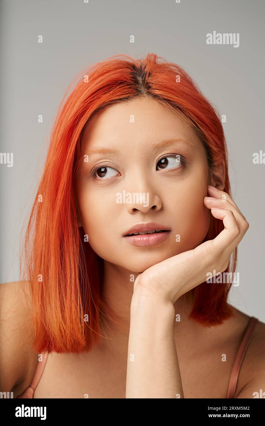 Porträt einer attraktiven und jungen asiatischen Frau mit perfekter Haut Tagträumerei auf grauem Hintergrund Stockfoto