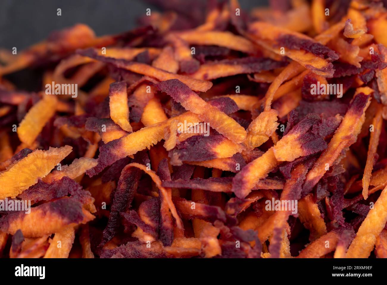 Fein geriebene rot-orangefarbene Karotten in der Küche, mehrere geschälte und gewaschene Karotten, die in Stücke gerieben wurden, auf einer Reibe Stockfoto