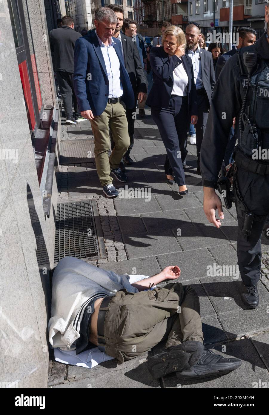 26. September 2023, Hessen, Frankfurt/Main: Nancy Faeser (SPD, M) Innenministerin und Spitzenkandidatin für die Landeswahl in Hessen geht an einem Mann vorbei, der auf der Bordsteinkante gegenüber einer Drogendruckkammer im Bahnhofsbezirk Frankfurt am Main liegt. Am 8. Oktober wird in Hessen ein neuer landtag gewählt. (Version mit modifiziertem Bildteil) Foto: Boris Roessler/dpa Stockfoto