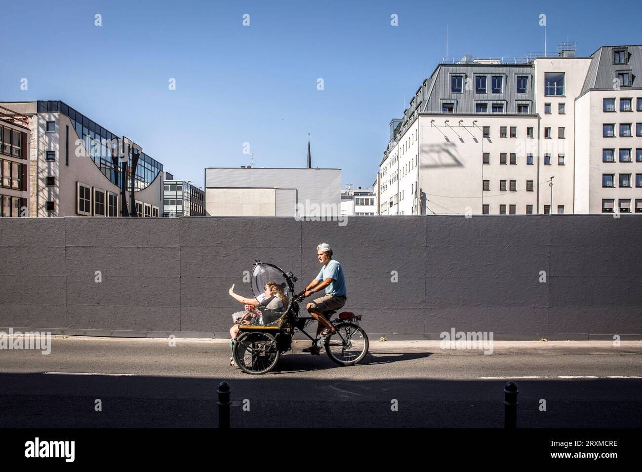 Ein Rikscha-Fahrer mit Touristen fährt an einem Bauzaun in der Nähe des Kölner Doms vorbei. ein Rikscha-Fahrer mit Touristen faehrt an einem Bauzaun Stockfoto