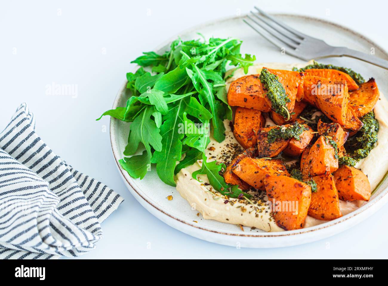 Veganes Mittagessen - Hummus, gebackene Süßkartoffel und Pesto, weißer Hintergrund, Nahaufnahme. Stockfoto