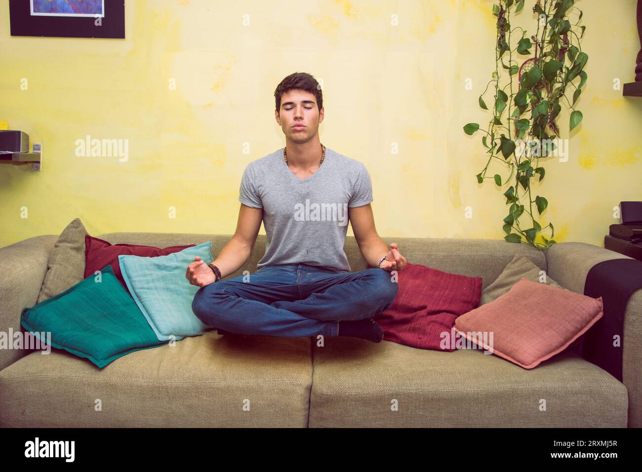 Ein Mann, der auf einer Couch in einer Yoga-Pose sitzt und magisch in der Luft schwebt Stockfoto