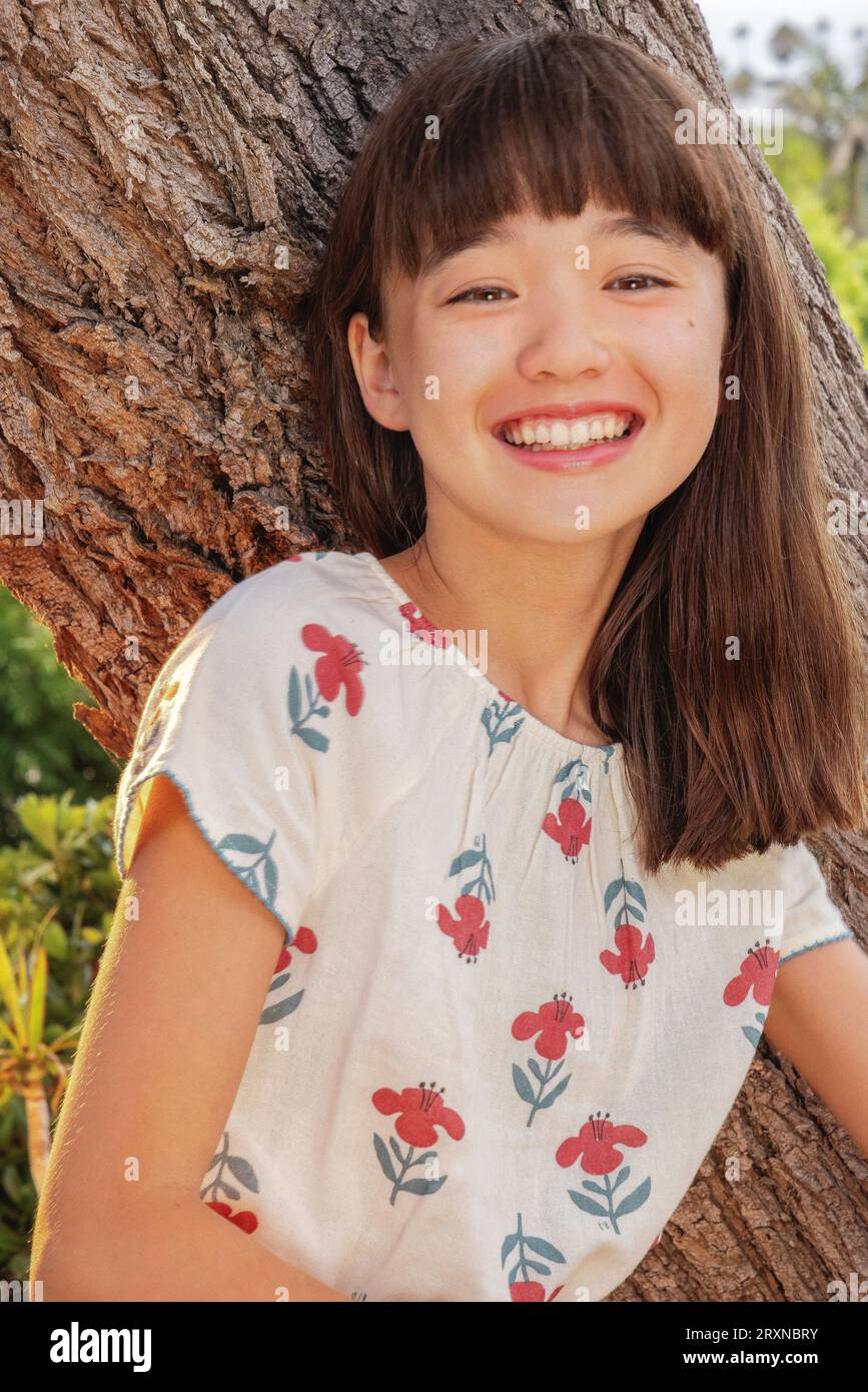 11-jähriges lachendes Mädchen, das sich an einen Baum lehnt Stockfoto