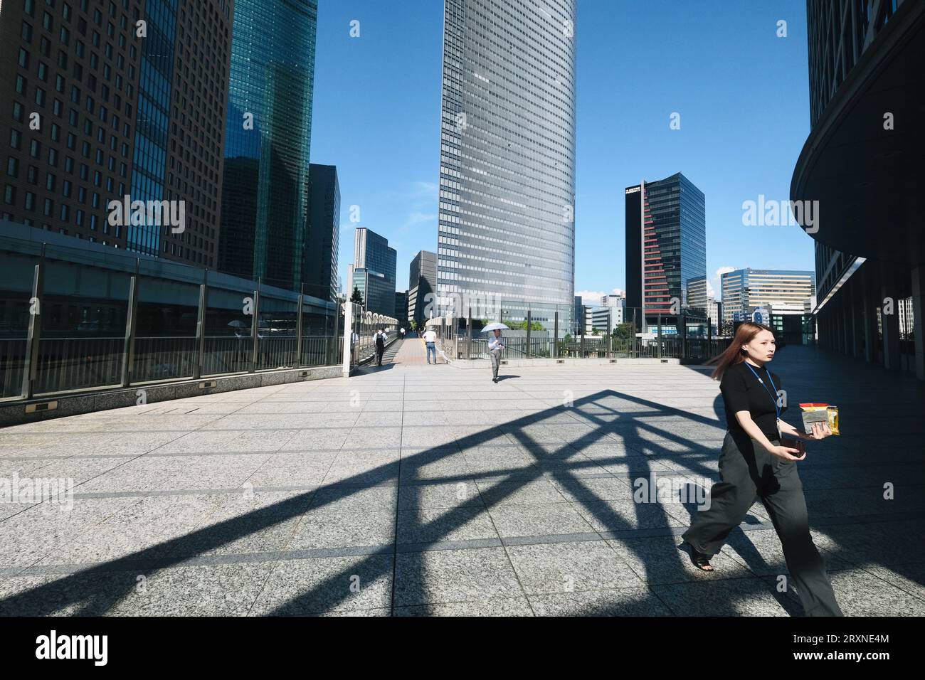 Eine Frau spaziert auf einem erhöhten Gehweg mit modernen Wolkenkratzern im Hintergrund in Shiodome, Tokio, Japan Stockfoto