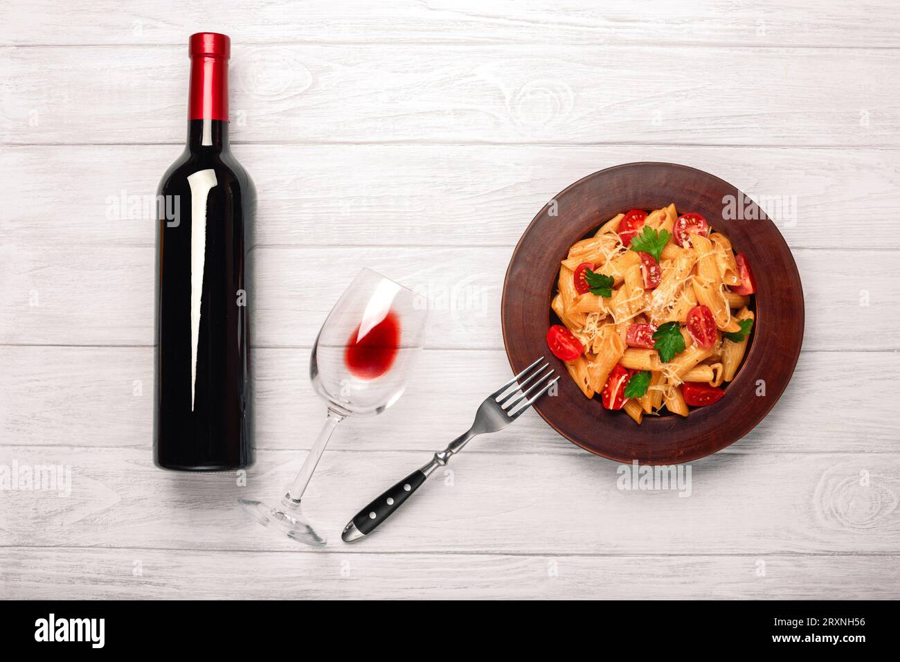 Pasta mit Käse, Kirschtomate, Weinglas und Flasche Wein auf weißen Holzbrettern, Blick von oben. Stockfoto