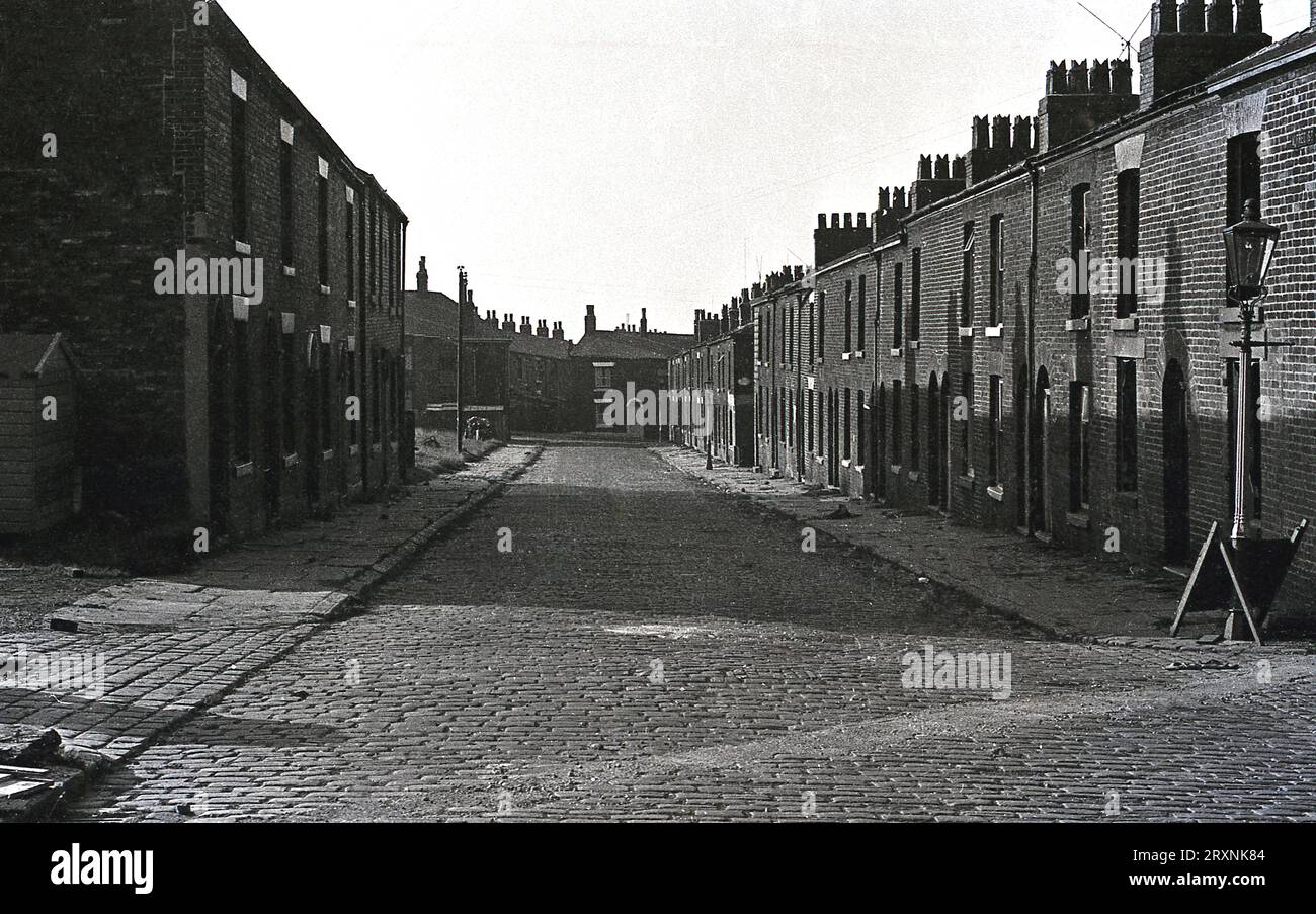 1960er Jahre, historische, kleine, flache Terrassenhäuser säumen eine Kopfsteinpflasterstraße, Arbeiterhäuser für die Arbeiter in den lokalen Textilfabriken Oldham, Lancashire, England, Großbritannien. Stockfoto