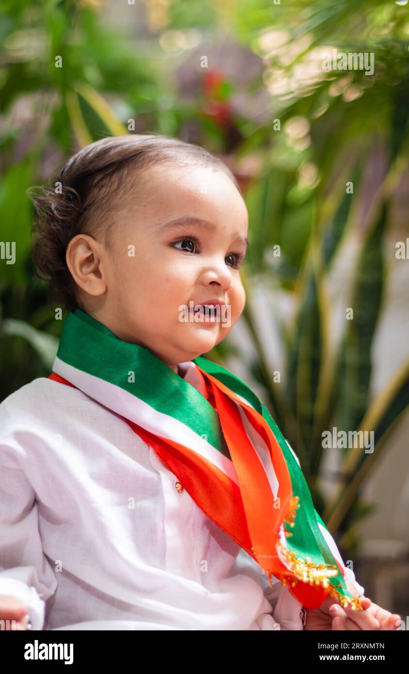 Niedliches Kleinkind mit indischer Trikolore-Flagge in traditionellem Tuch mit unschuldigem Gesichtsausdruck Stockfoto