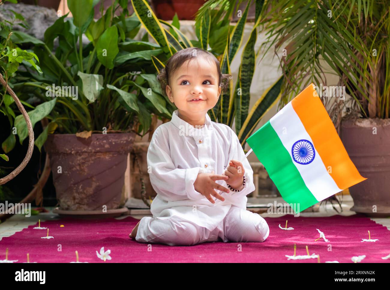Niedliches Kleinkind mit indischer Trikolore-Flagge in traditionellem Tuch mit unschuldigem Gesichtsausdruck Stockfoto