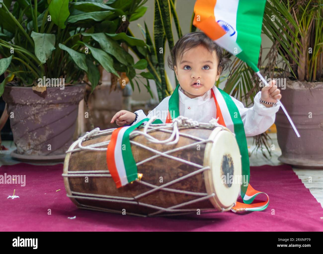 Niedliches Kleinkind mit indischer Trikolorfahne, traditionellem Dholak und Tuch mit unschuldigem Gesicht Stockfoto