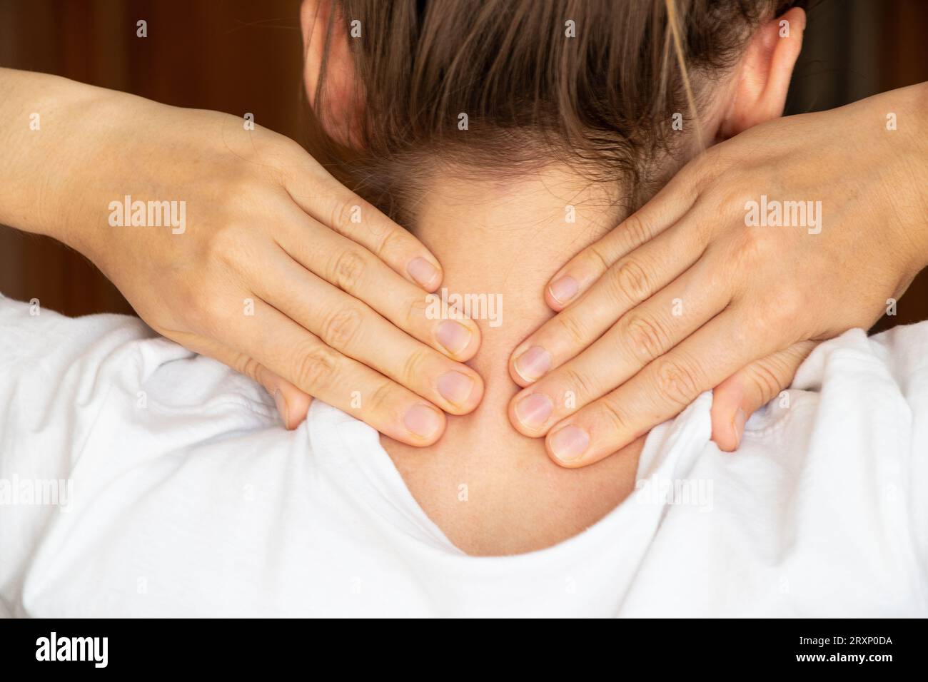 Ein Mädchen hält ihre Hände zu Hause hinter dem Hals, Halsschmerzen, akute Nackenschmerzen Stockfoto