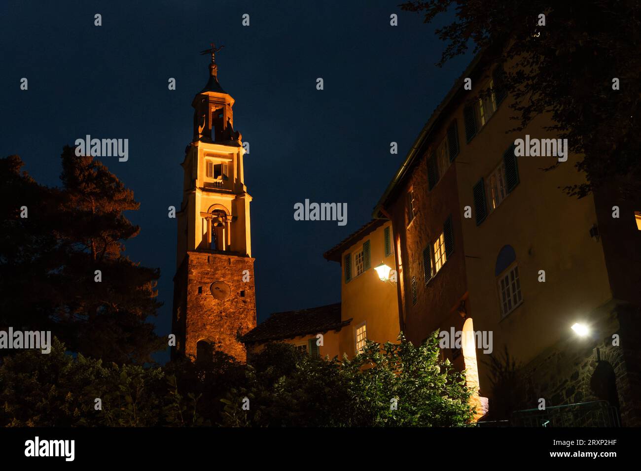 Beleuchteter Uhrenturm und farbenfrohe Gebäude in der Abenddämmerung im Dorf Portmeirion, Wales Stockfoto