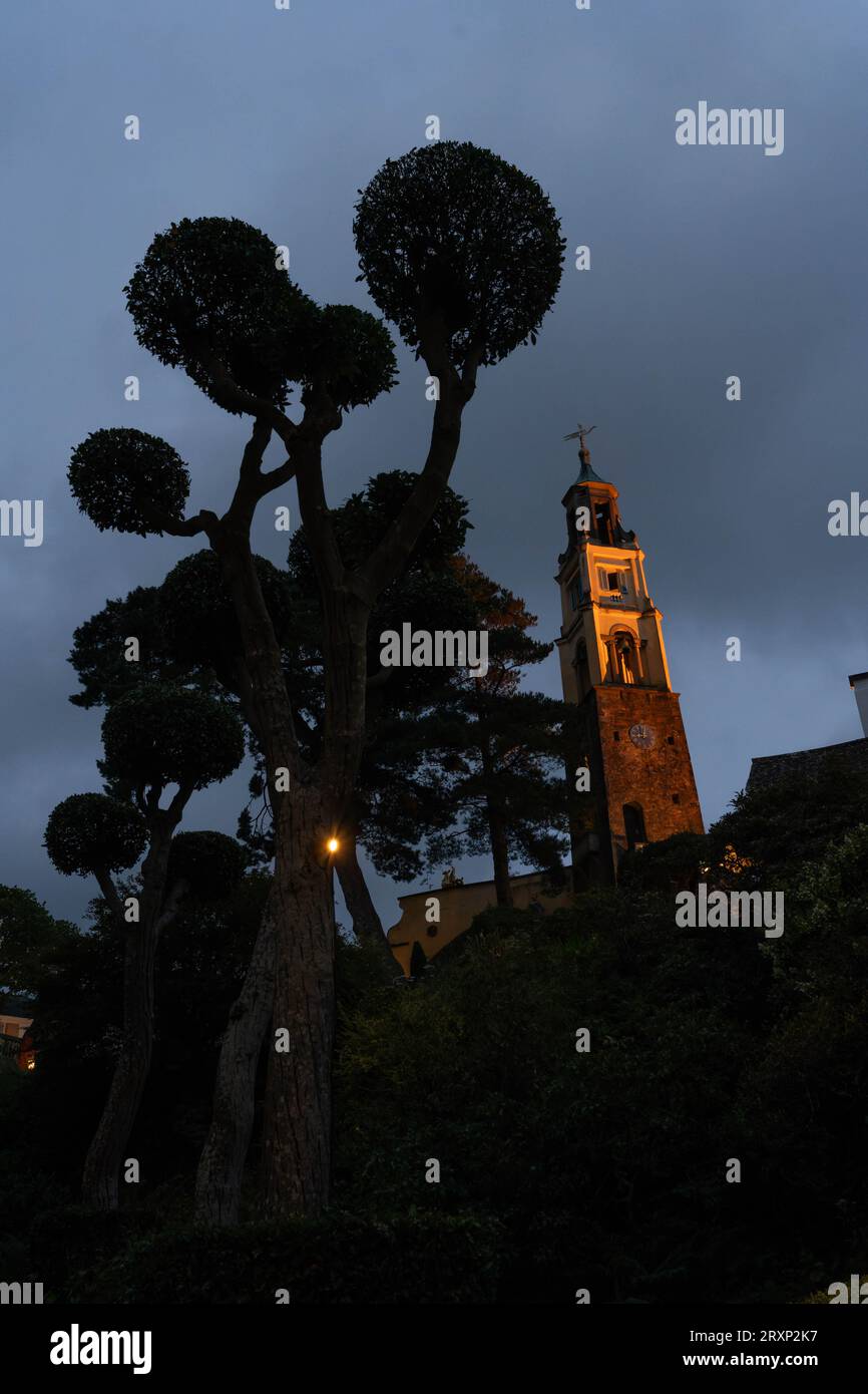 Beleuchteter Glockenturm und Formbäume in der Abenddämmerung im Dorf Portmeirion Wales Stockfoto