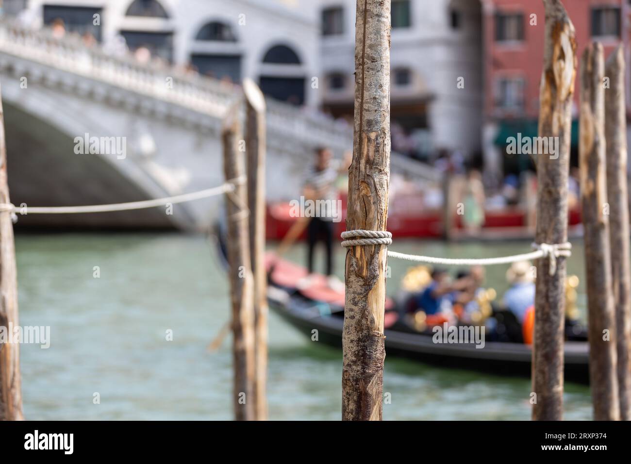 Blick auf die Anlegepfähle des Großen Kanals von Venedig mit verschwommener Gondel im Hintergrund und Rialto-Brücke Stockfoto