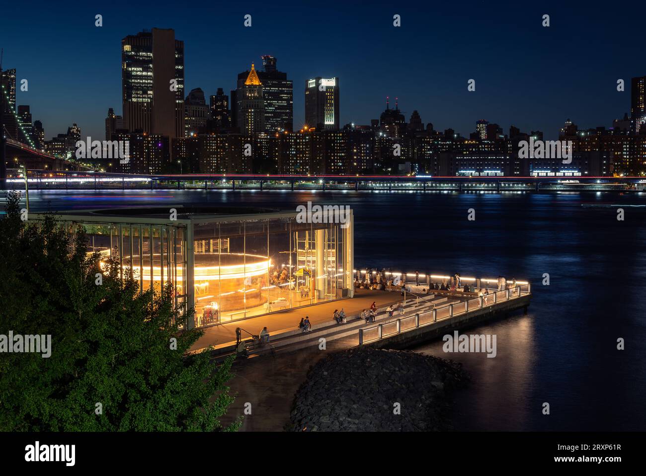 Einzigartiger Blick auf das Jane's Karussell im Brooklyn Bridge Park in Blue Hour. Manhattan's Two Bridges Area und East River im Vordergrund. Stockfoto