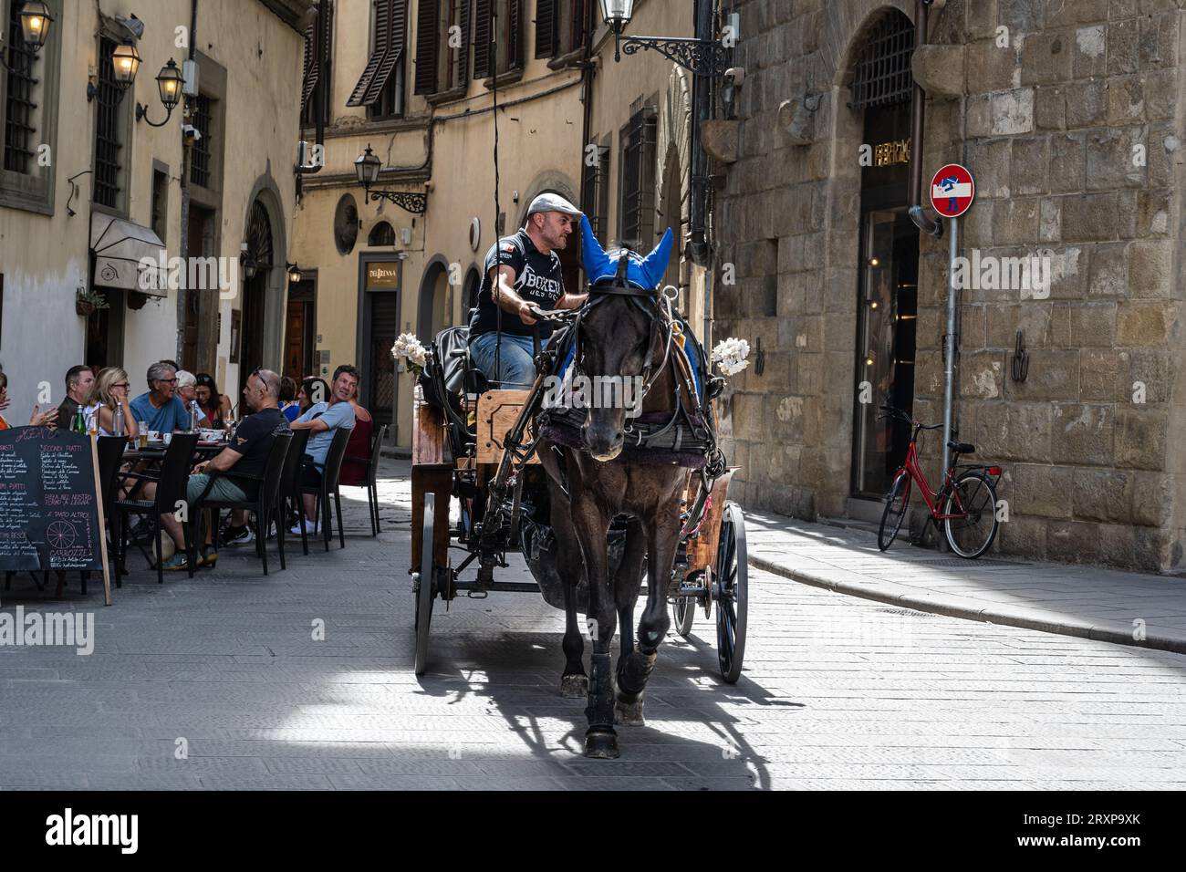 Florenz, Italien – 3. September 2023. Ein Foto von einem Pferd, einer Kutsche und einem Fahrer, der an einem Restaurant im Freien in einer Seitenstraße in der Innenstadt von Florenz, Italien, vorbeitrottelt Stockfoto