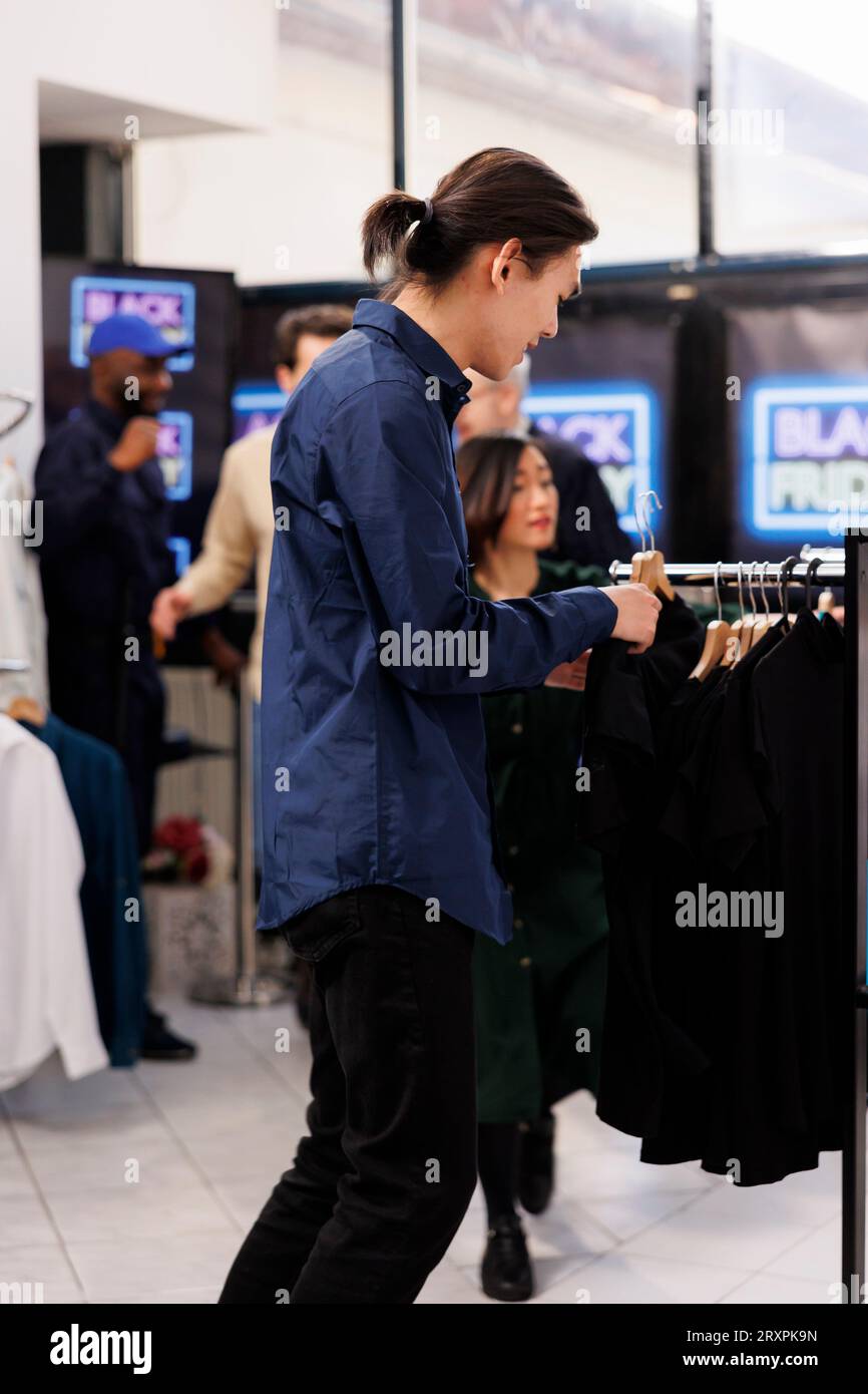 Verschiedene Leute, die in einem Bekleidungsgeschäft einkaufen, um Black Friday-Angebote zu erhalten und Kleidung zu ermäßigten Preisen zu kaufen. Schnäppchenjagd und Einkaufssucht, saisonales Verkaufskonzept Stockfoto