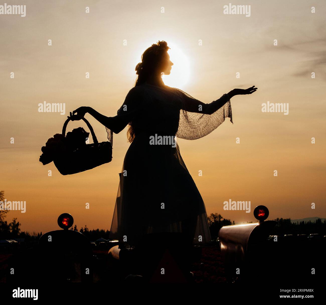 Silhouette einer Frau, die gegen die untergehende Sonne steht, mit dem Korb in der Hand Stockfoto