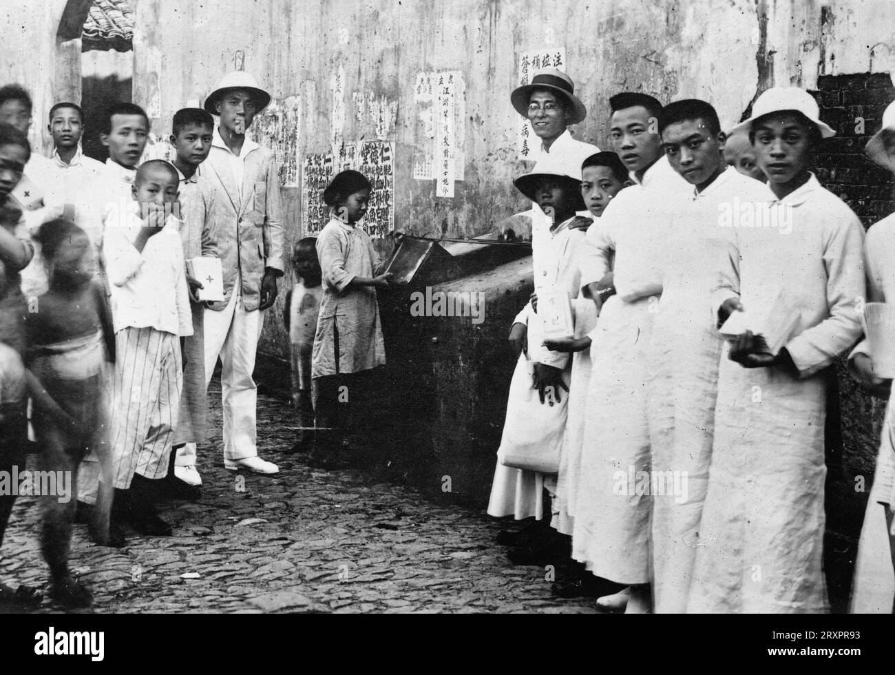 Chinesische Rotkreuz-Junioren, die Flugblätter über die Verhütung von Cholera verteilen und auf die ordnungsgemäße Entsorgung von Müll drängen, in Zementbehältern, die bereits von der Stadt bereitgestellt werden. Shanghai, China, August 1919 Stockfoto