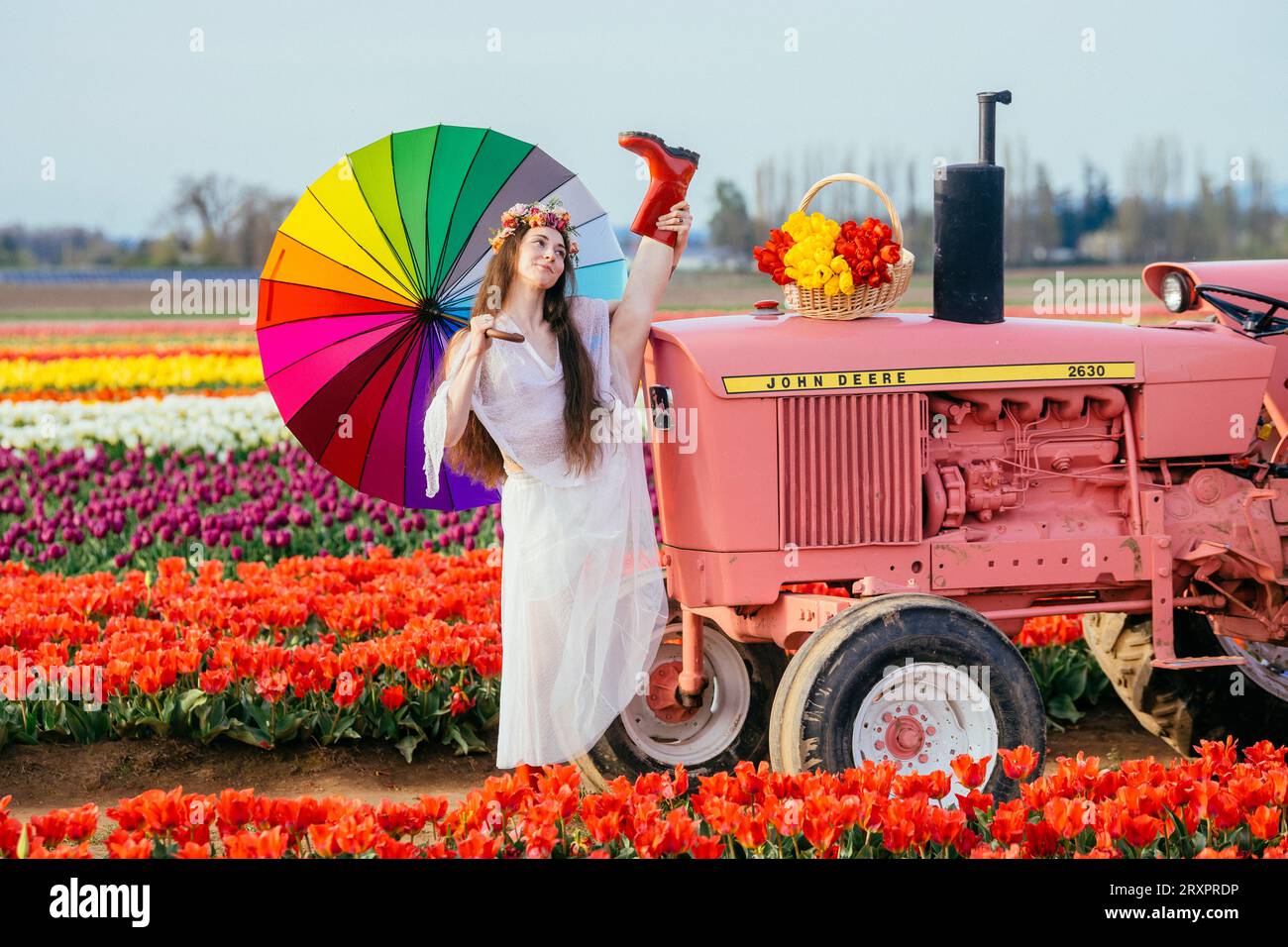Frau, die einen bunten Regenschirm hält und sich auf dem rostigen Traktor teilt Stockfoto