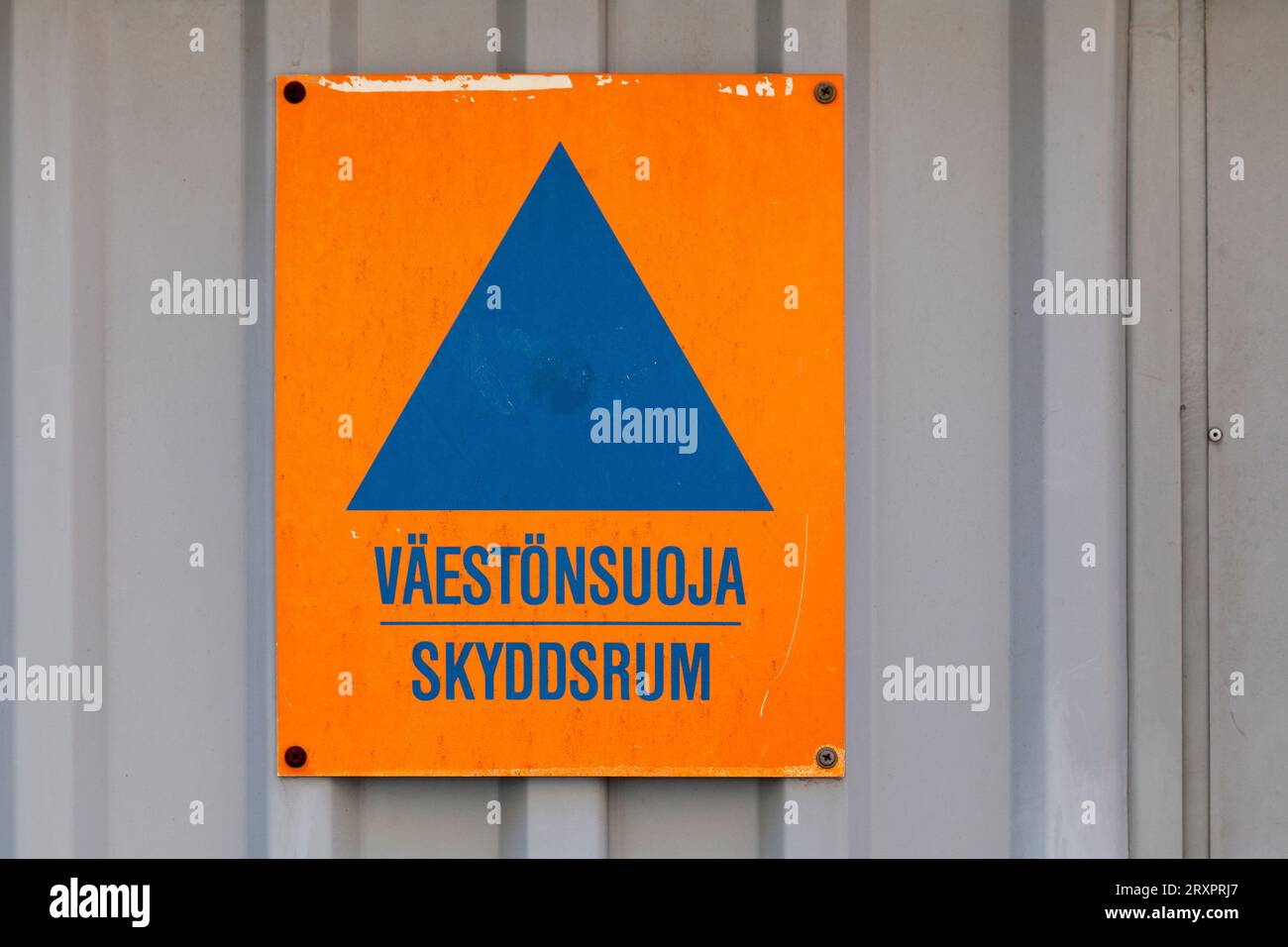 Blaues Dreieck auf einem orangefarbenen Schild mit der Aufschrift „Väestönsuoja skyddsrum“, was auf Englisch „Luftschutzbunker“ bedeutet. Stockfoto