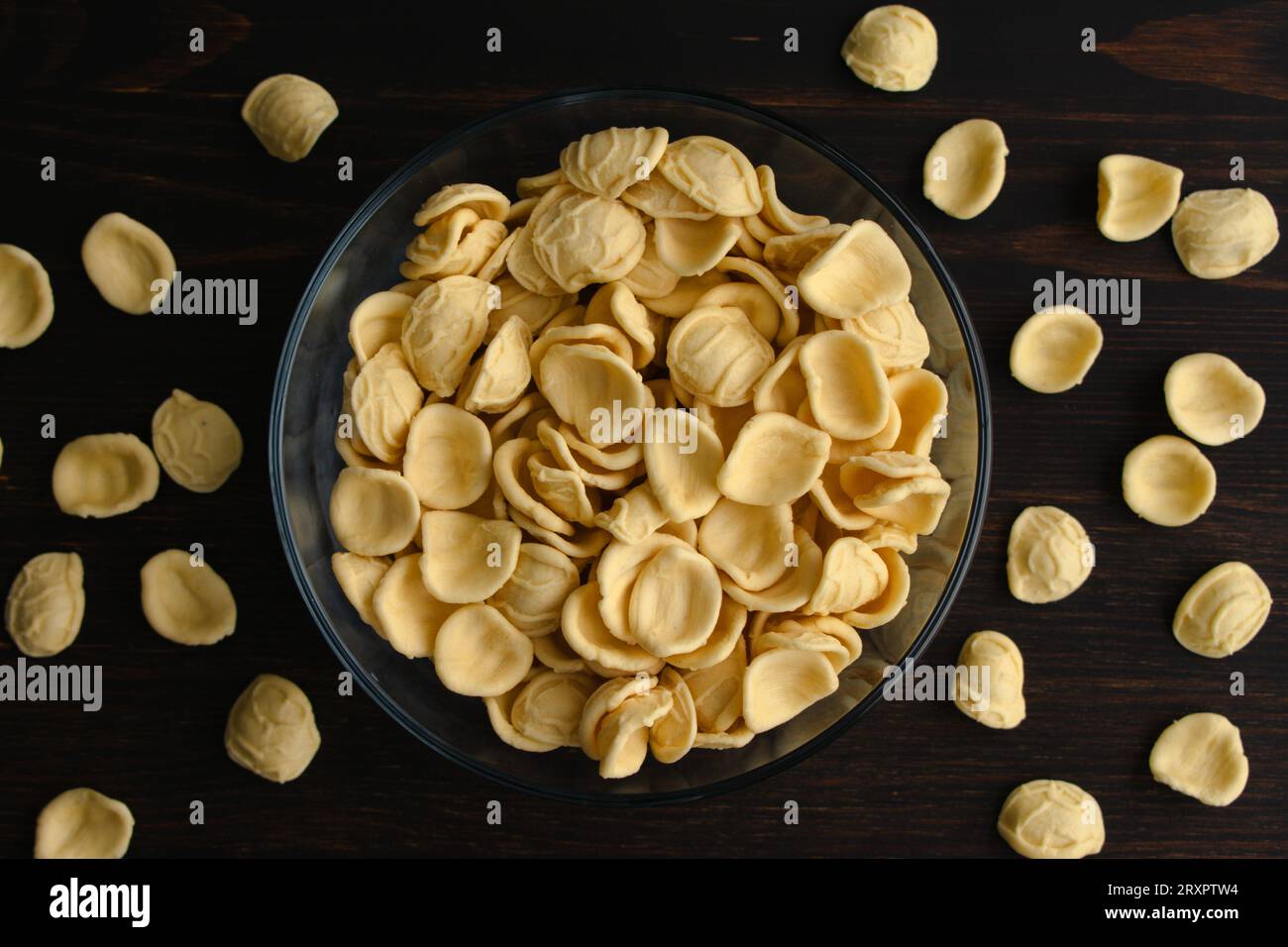Getrocknete gelbe Orecchiette-Pasta in einer Glasschale: Eine Schüssel ungekochter Orecchiette-Pasta auf einem Holztisch von oben gesehen Stockfoto