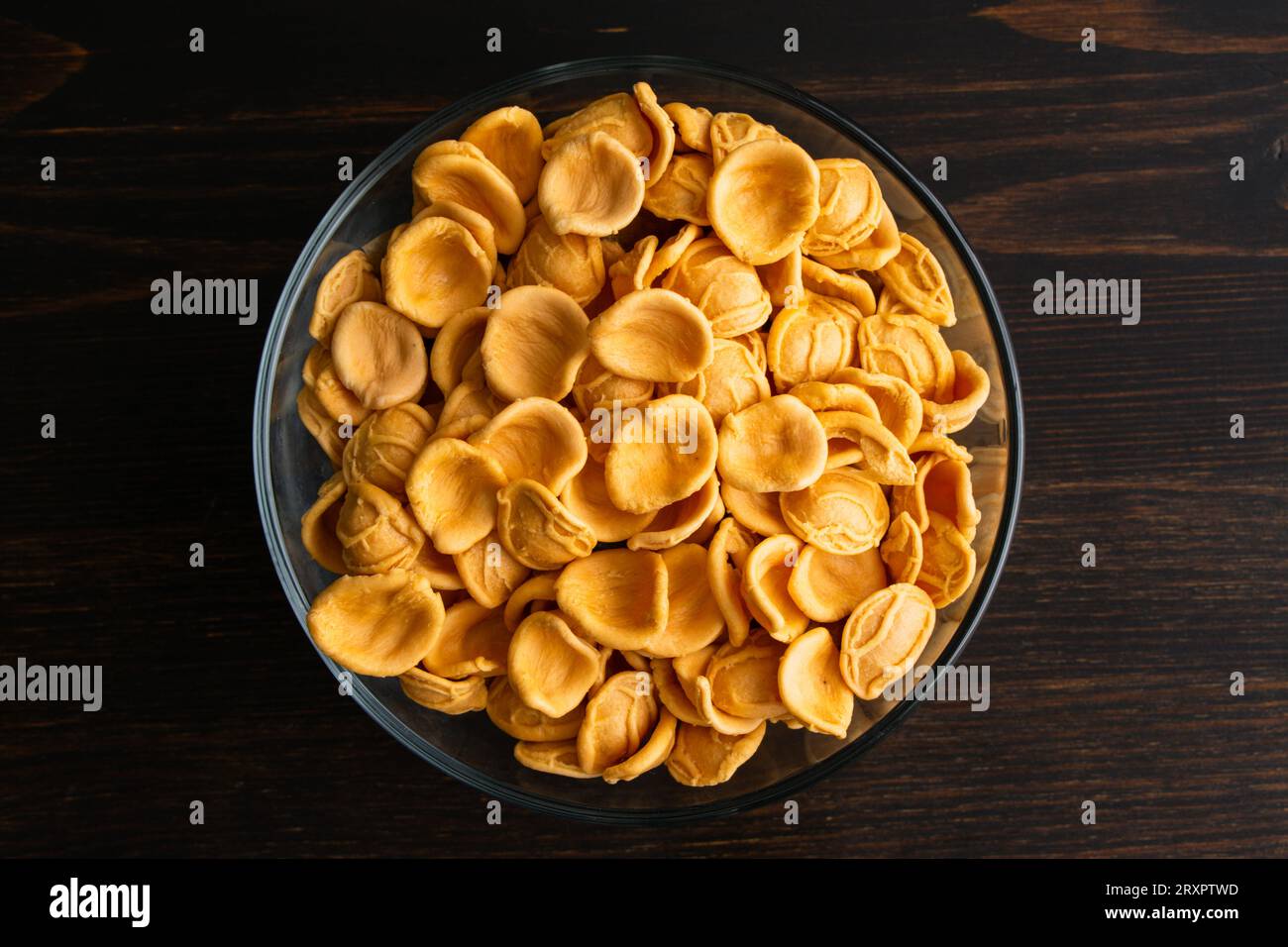 Getrocknete Orangen-Orecchiette-Pasta in einer Glasschale: Eine Schüssel ungekochter Orecchiette-Pasta auf einem Holztisch von oben gesehen Stockfoto