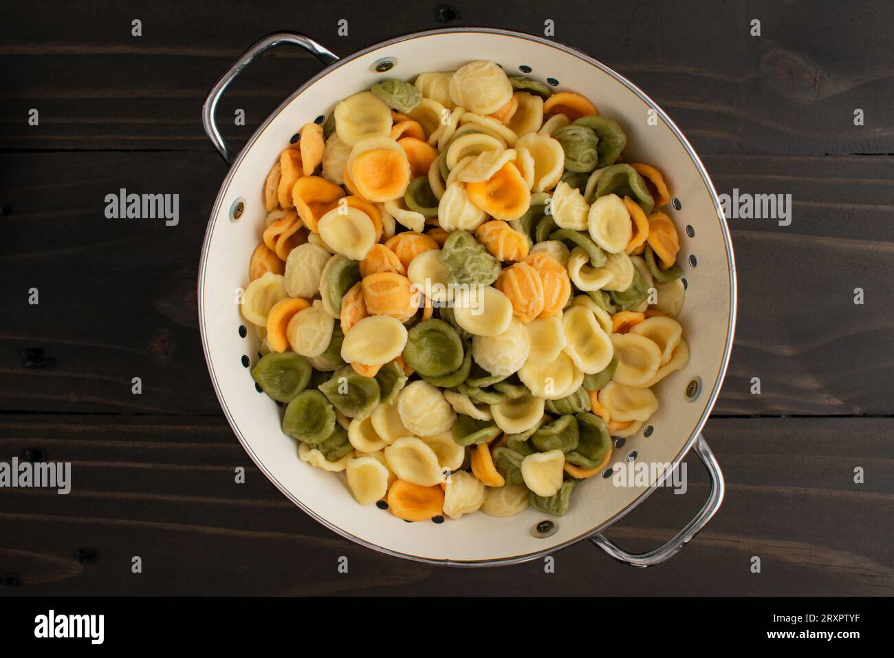 Gekochte und abgetropfte dreifarbige Orecchiette-Pasta in einem Sieb: Gekochte und abgetropfte gelbe, orange und grüne Orecchiette-Pasta von oben gesehen Stockfoto