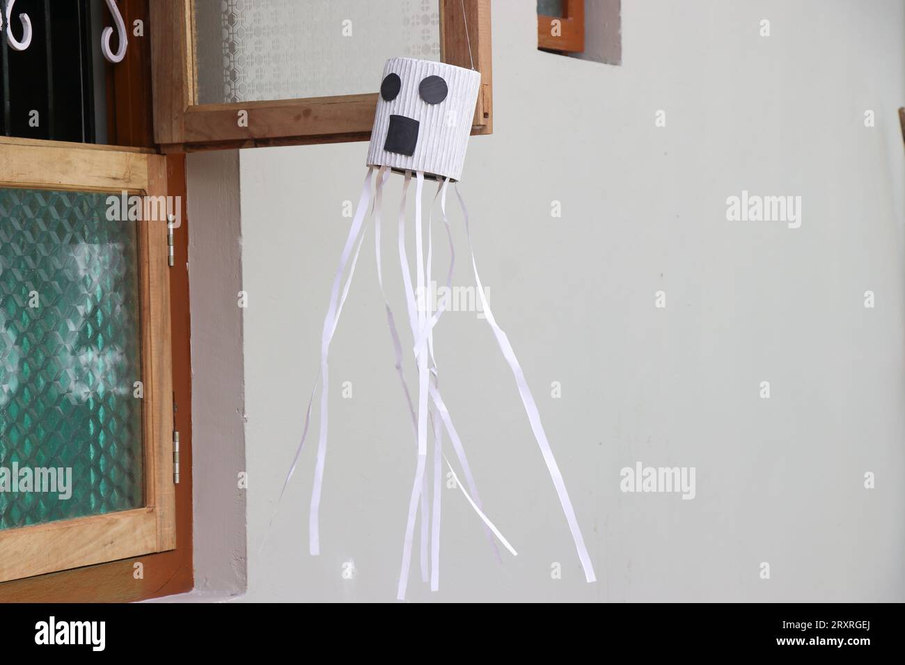 Das Halloween-Dekor-Konzept wird durch eine Figur dargestellt, die an einem Fenster in einem Haus hängt Stockfoto