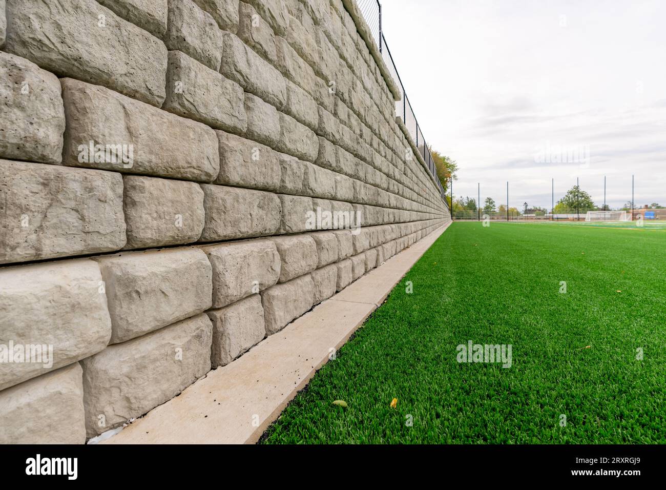 Stützwand neben einem grünen Kunstrasen-Sportfeld. Stockfoto