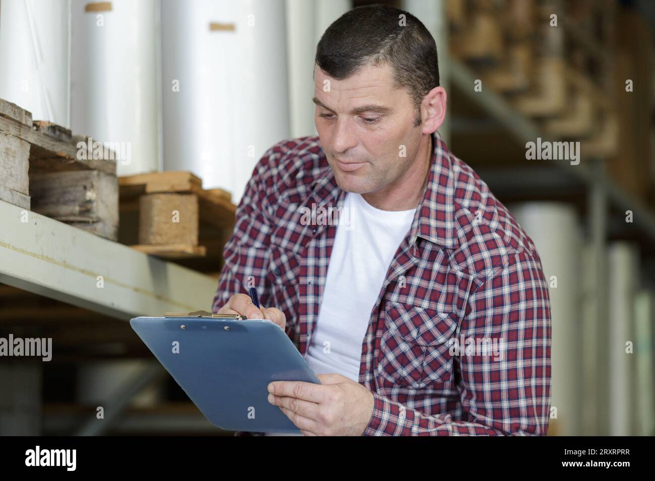 Reifer Mann im Lager, der eine Zwischenablage hält Stockfoto