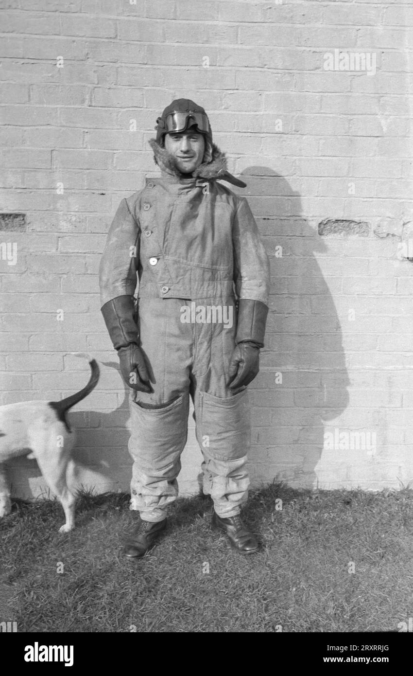 Ein klassisches Schwarz-weiß-Foto aus den 1930er Jahren, das einen britischen Flieger in einem historischen Fliegeranzug zeigt, der vor seinem Haus steht. Stockfoto