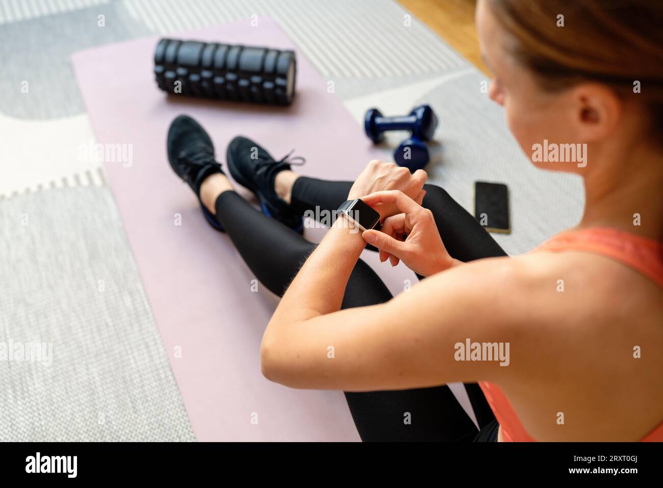 Sportliche Frau, die Sportbekleidung trägt Frau sitzt auf der Trainingsmatte und startet das Trainingsprogramm auf ihrer Smartwatch. Fitness und persönliche digitale Geräte. Stockfoto