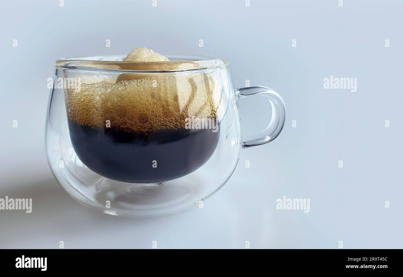 Nahaufnahme von schwarzem Kaffee mit Naturschaum in doppelwandigem transparentem Glas mit einfachem Hintergrund, Morgenboost, Espresso, Americano, dunkel geröstet, RO Stockfoto