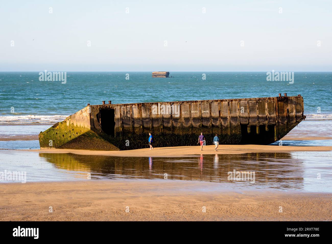 Die Menschen spazieren am Strand neben den Überresten des Mulberry-Hafens, der nach den Landungen in der Normandie im Zweiten Weltkrieg am Gold Beach in Arromanches, Frankreich, errichtet wurde. Stockfoto